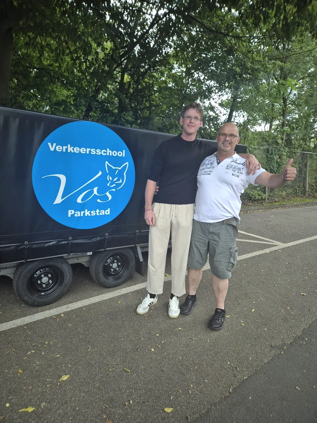 Twee mannen met de duim omhoog bij de aanhanger van Verkeersschool Vos Parkstad