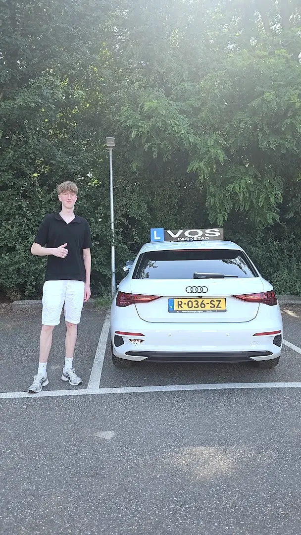 Geslaagde jongen naast de witte lesauto