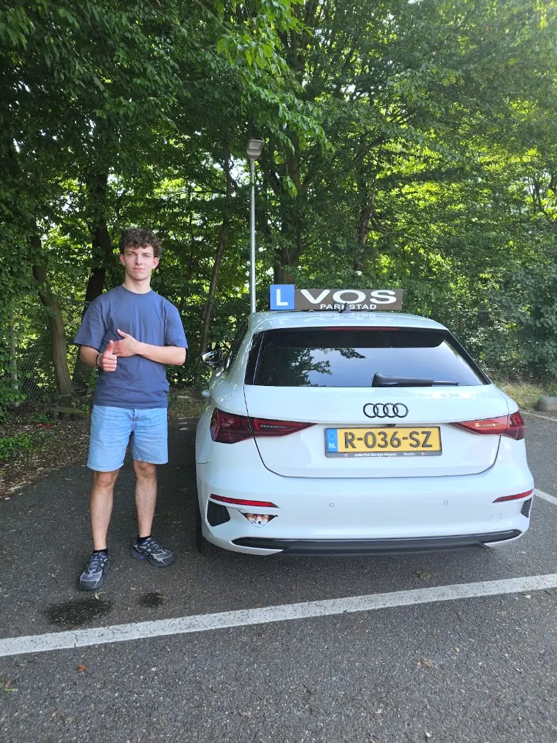 Geslaagde jongen met de duim omhoog naast de witte lesauto