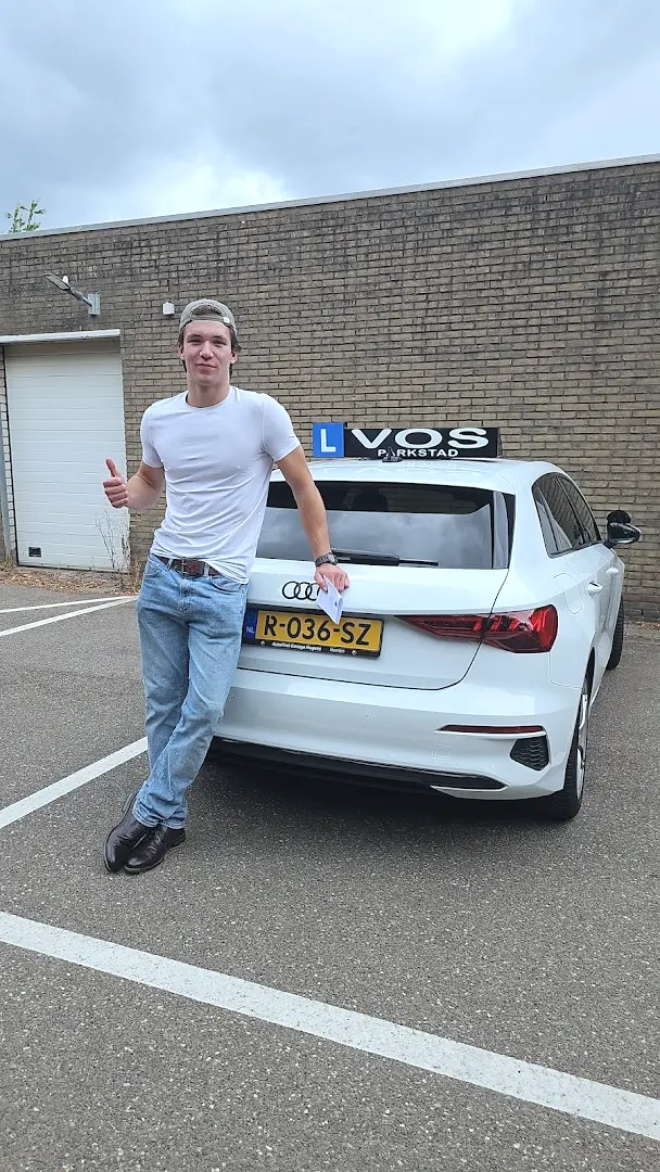Geslaagde jongen met de duim omhoog tegen de witte lesauto