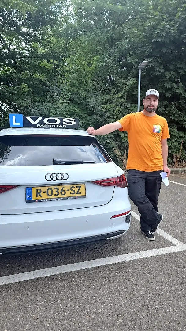 Geslaagde man in oranje shirt naast de witte lesauto